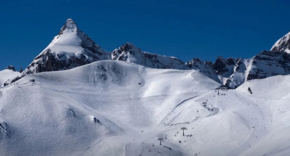 A snowy peak and a wide slope with chairlifts under a deep blue sky