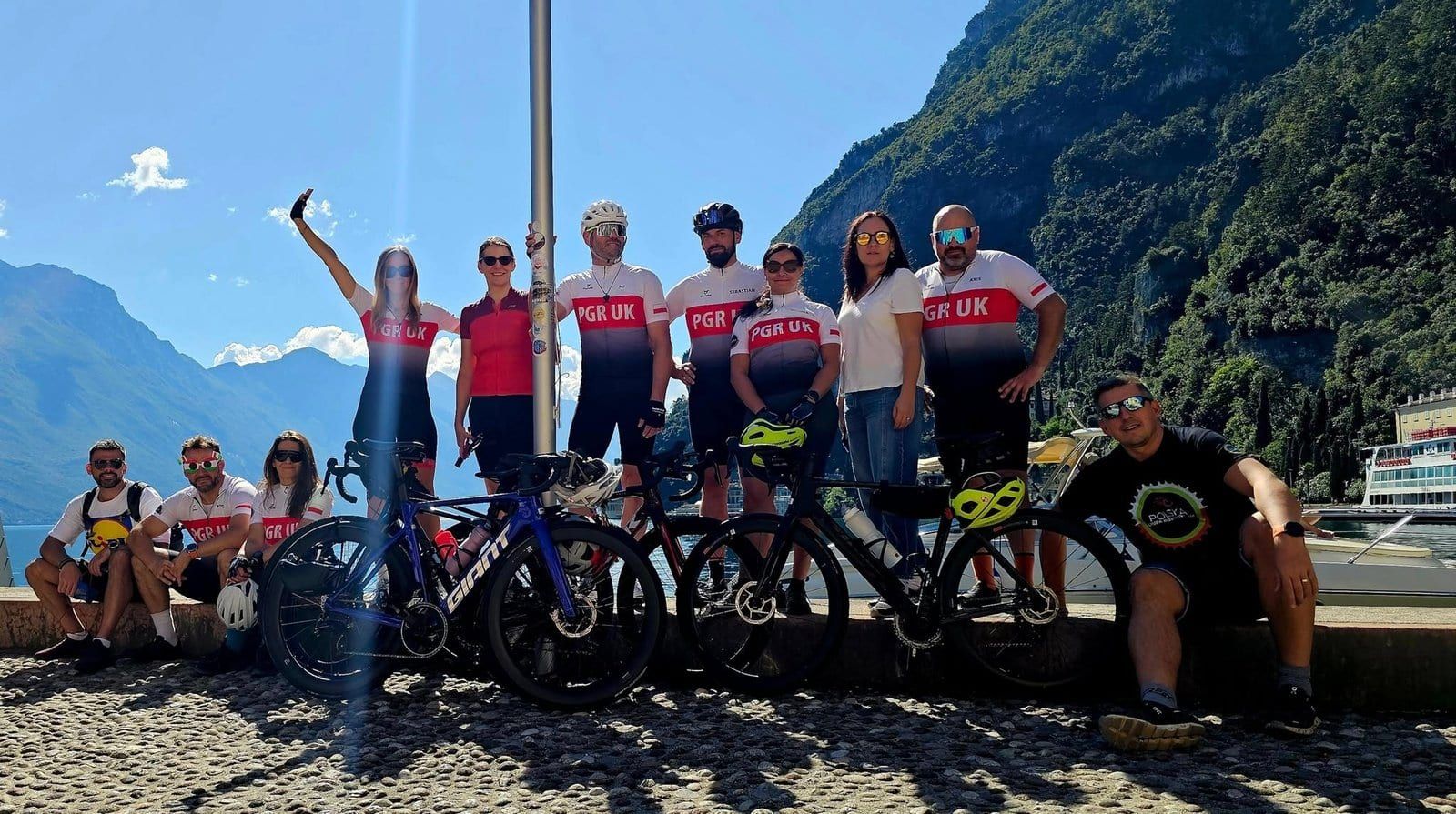 A group of cyclists on a lakeside quay with steep slopes behind