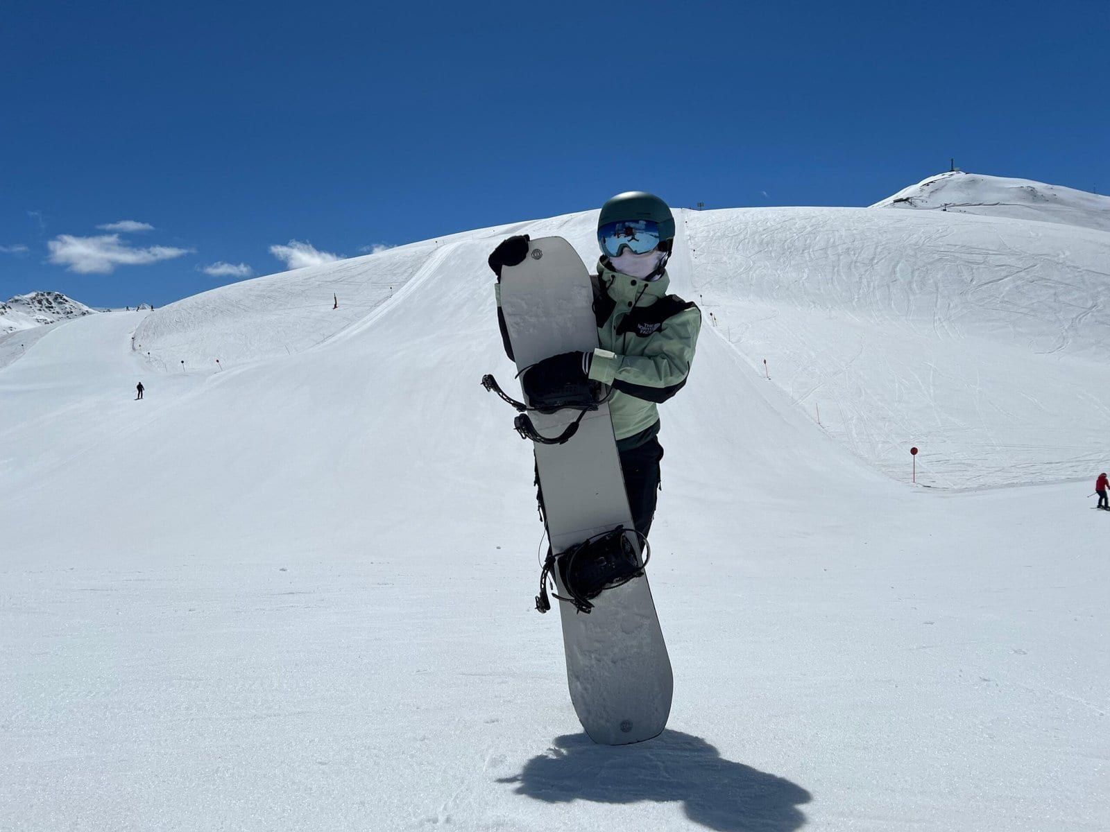 Beata holding a snowboard on a wide, sunny slope