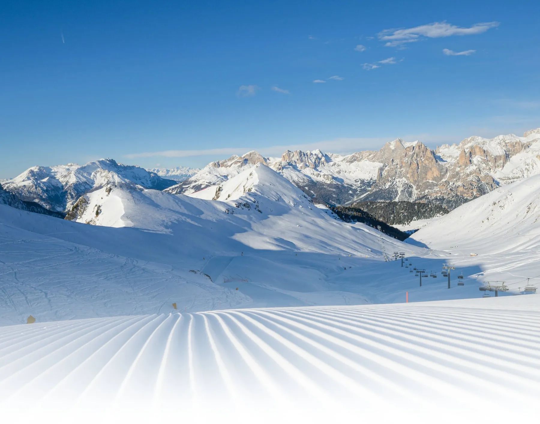 Snowy Dolomites and a freshly groomed slope with corduroy stripes on a sunny day